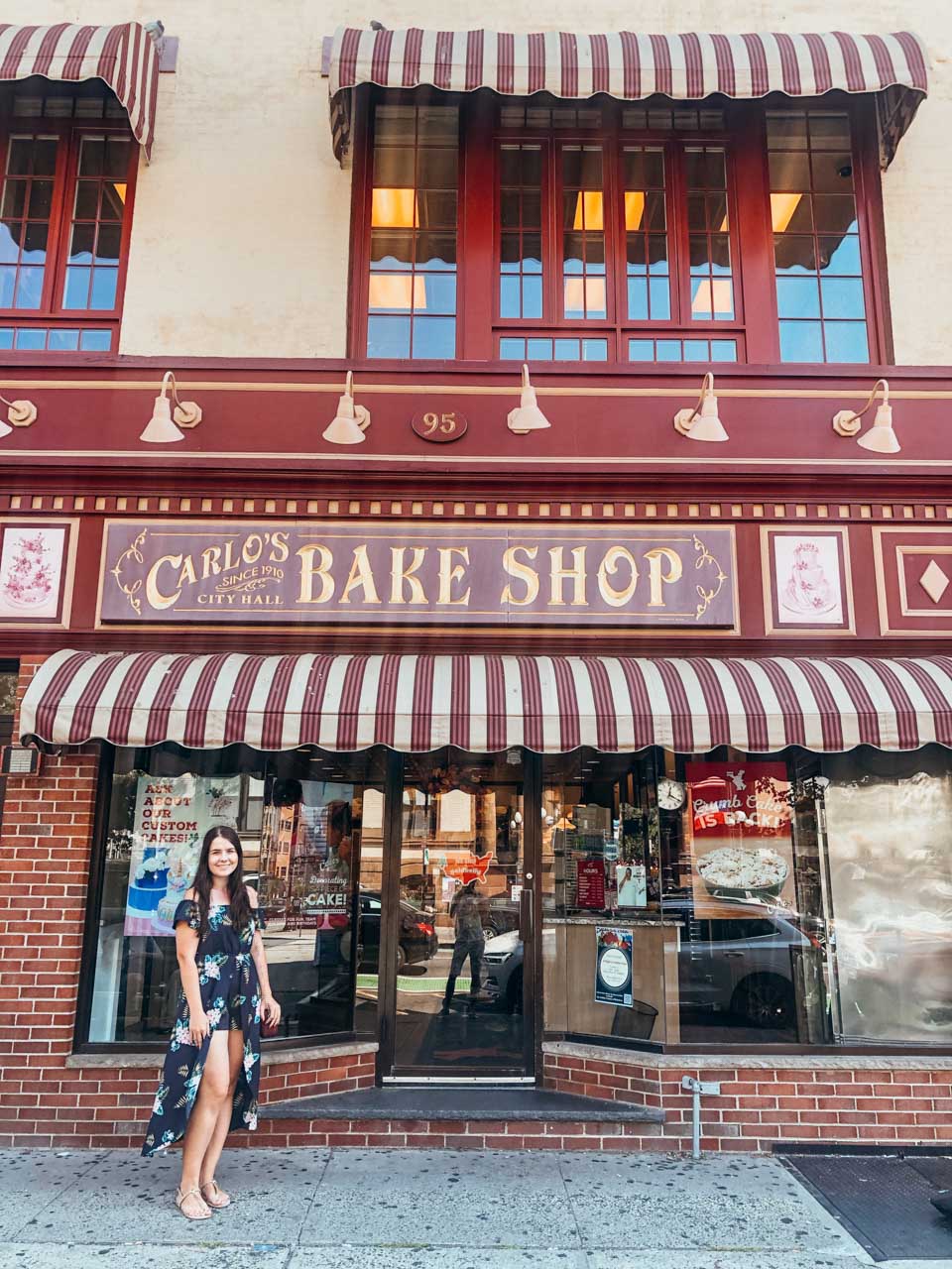 A girl in a floral dress standing outside Carlo's Bake Shop in Hoboken, New Jersey