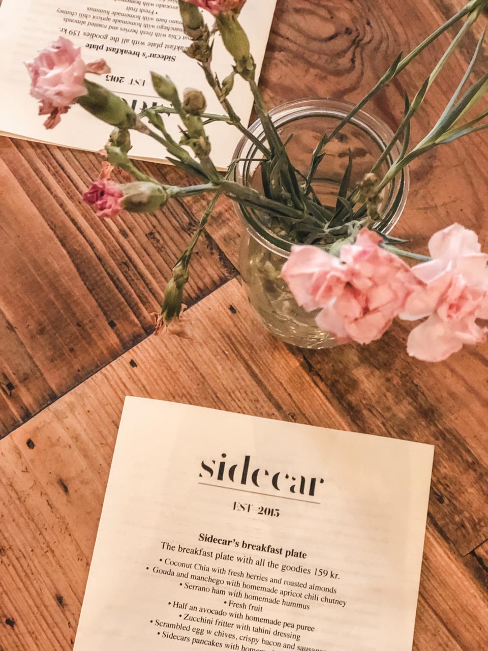 Two menus and a vase filled with flowers inside Sidecar in Copenhagen, Denmark