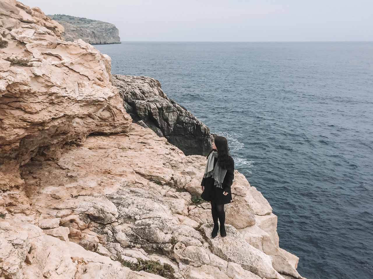 A girl in a coat standing close to the Blue Grotto, Malta