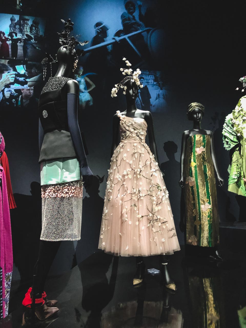 A blush tulle Dior gown with trailing cherry blossoms next to other Dior dresses on display