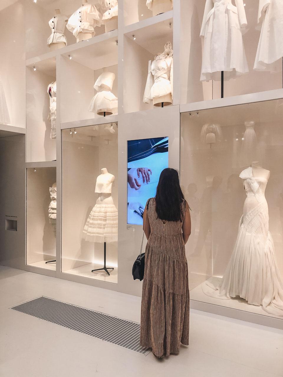 A girl looking at a floor-to-ceiling display of white garment prototypes at a Dior atelier