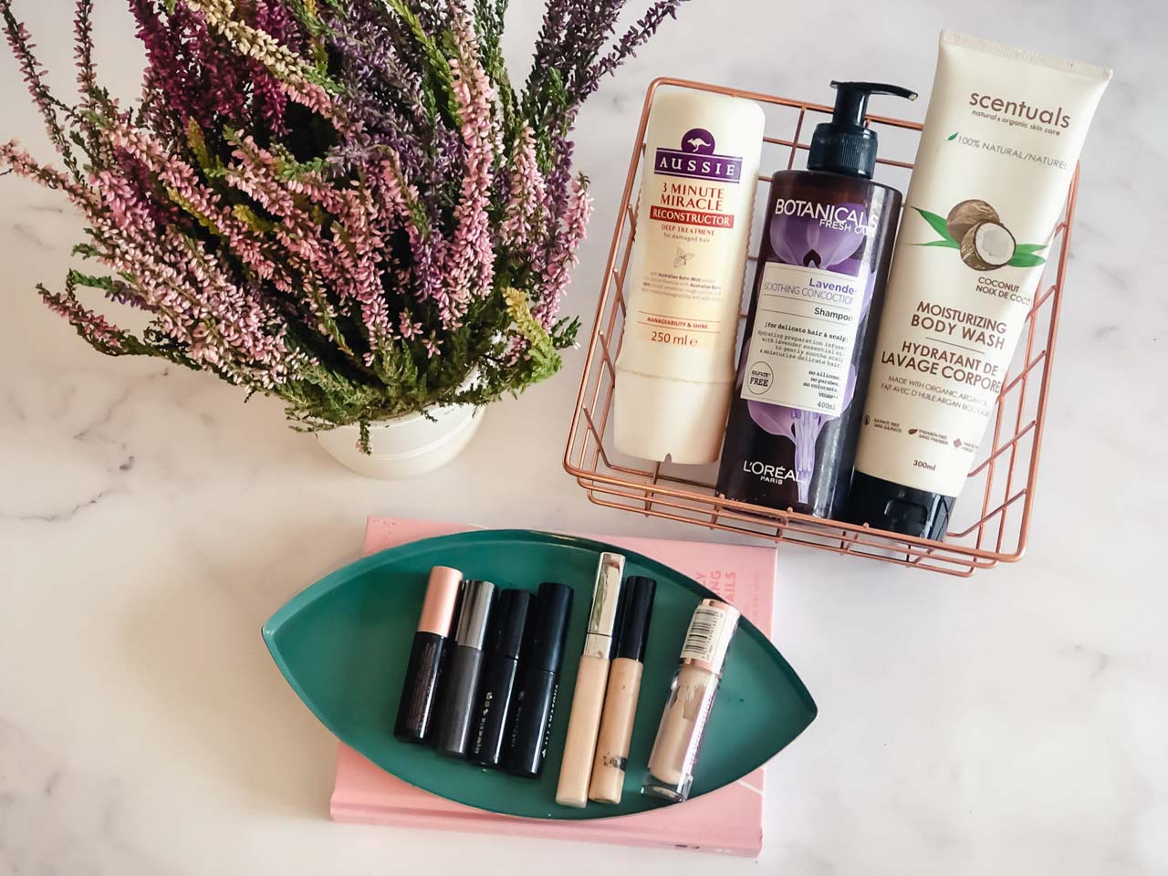 Makeup, skincare, hair and bath products displayed on a marble desk next to a heather plant