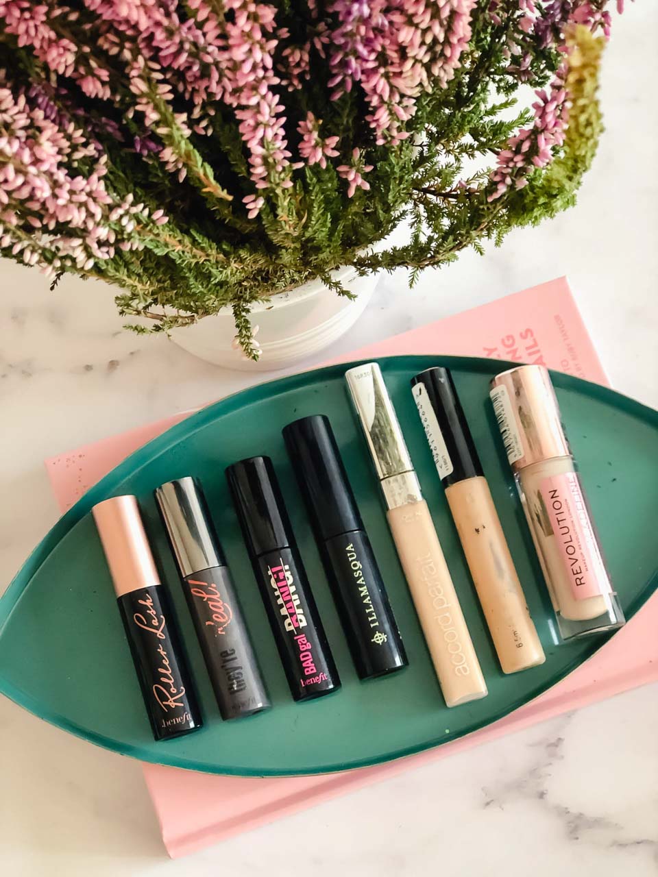 Makeup products displayed on a marble desk in front of a heather plant
