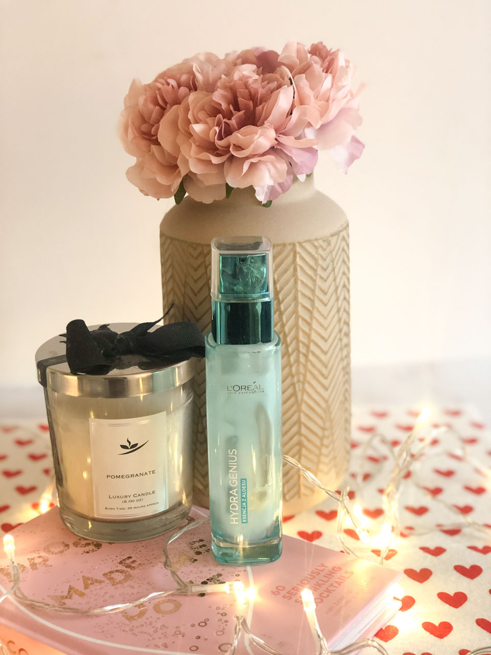 L'Oreal Hydra Genius moisturiser on a desk next to a candle and a vase with peonies