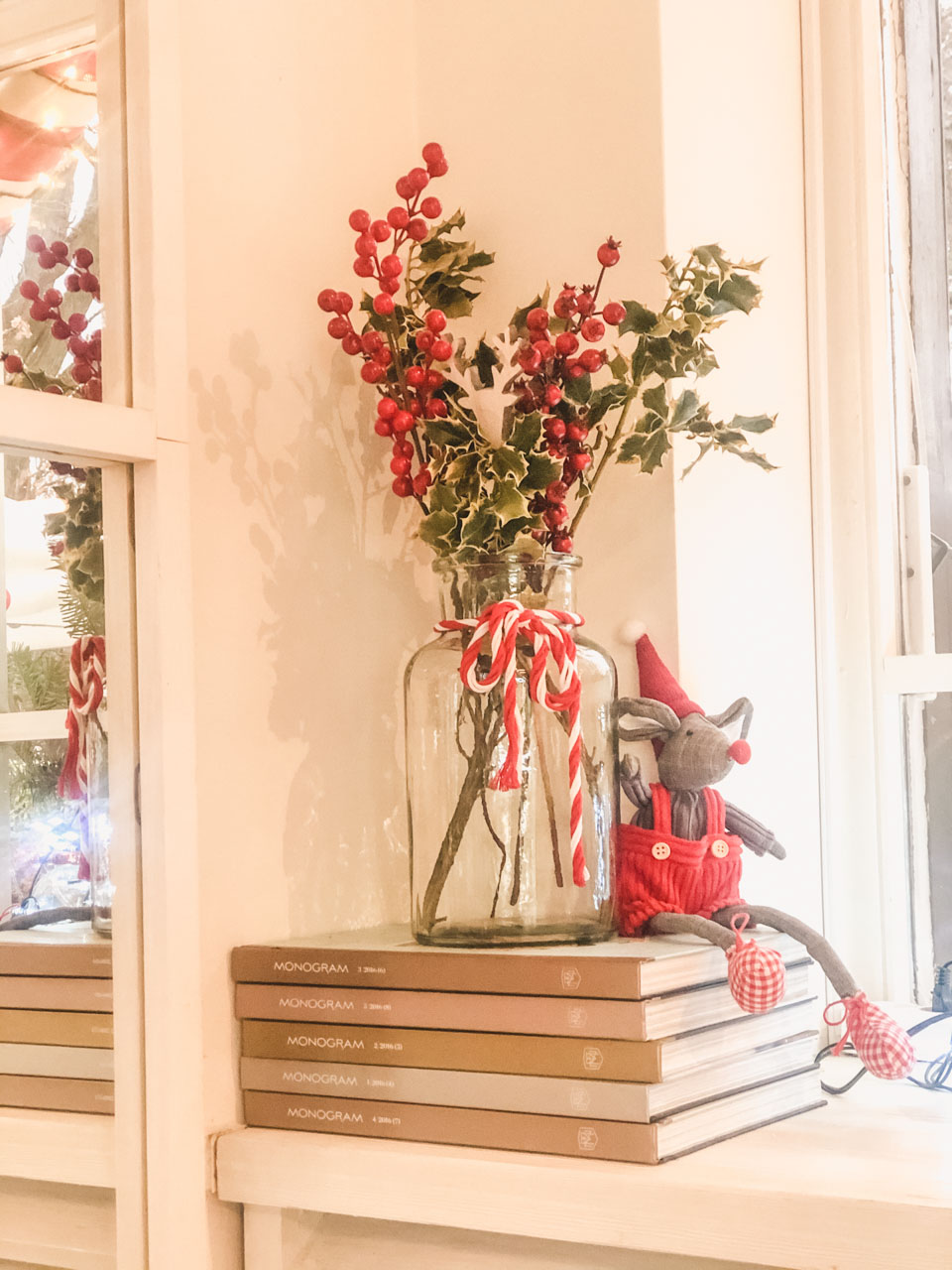 A vase with holly and a mouse toy on a stack of books