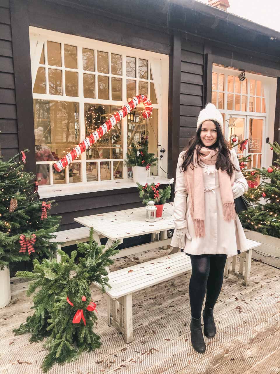 A girl in a white coat standing in front of Christmas trees and a decorative candy cane