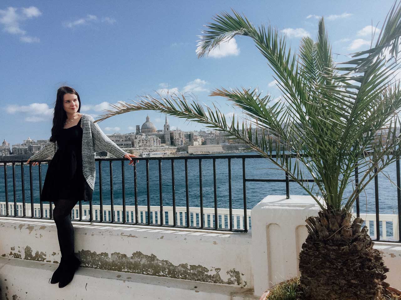 A girl standing on the promenade in Sliema, Malta with the Valletta skyline in the background