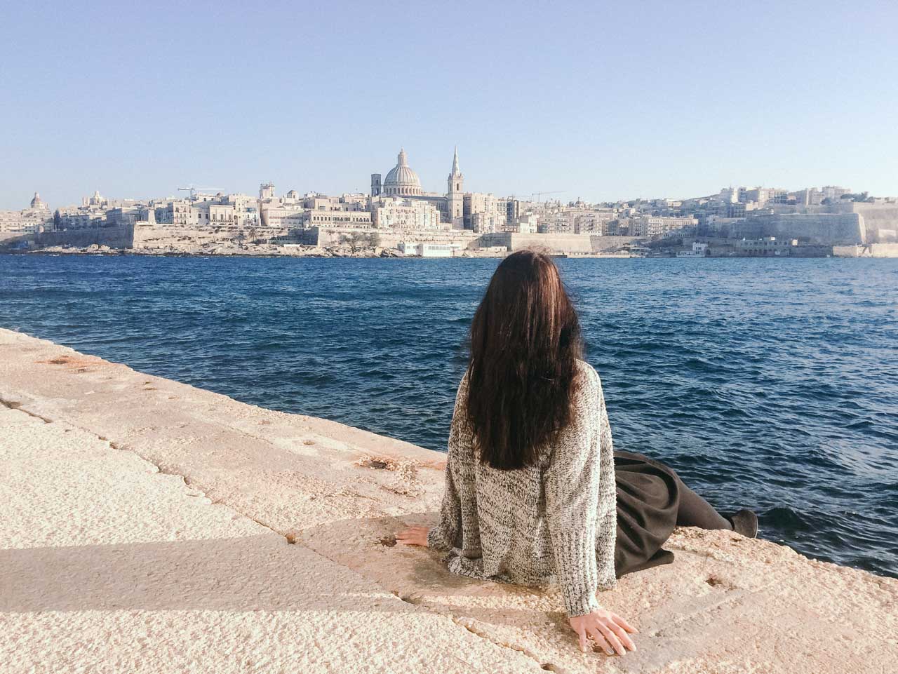 A girl sitting on the waterfront in Sliema, Malta overlooking Valletta