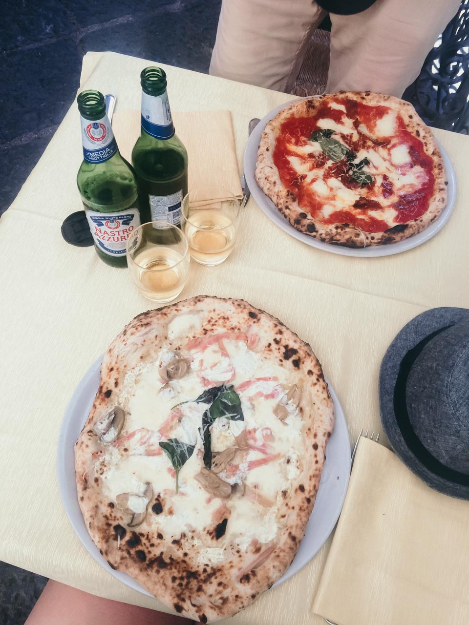 A bird's eye shot of two pizzas and two bottles of beer on a table