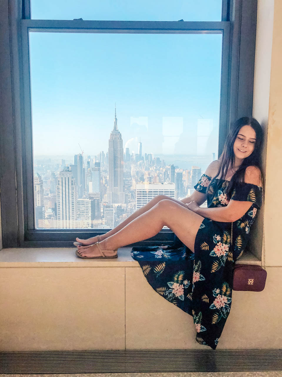 A girl sitting on a windowsill of the Top of the Rock observation deck