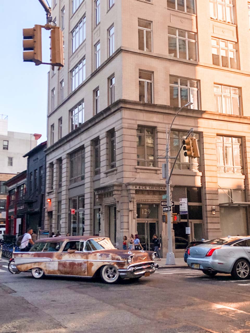 An old rusty car driving down the street in New York City