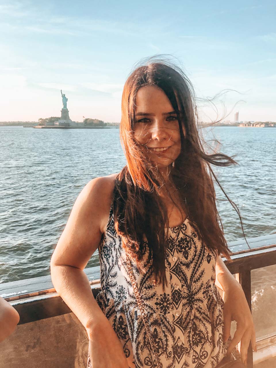 A girl standing on board of the Staten Island ferry with the Statue of Liberty in the background