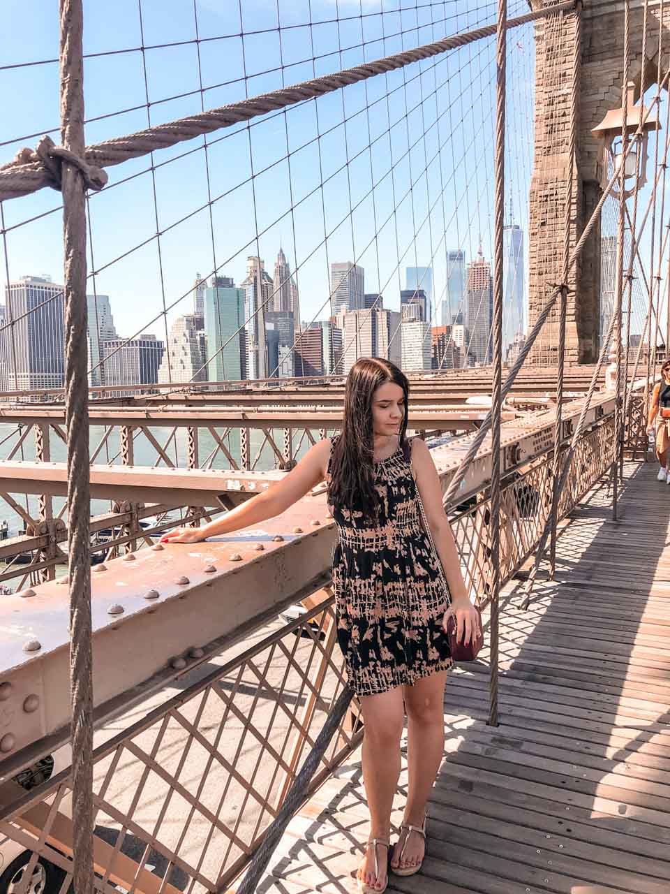 A girl standing on the Brooklyn Bridge with the Manhattan skyline in the background