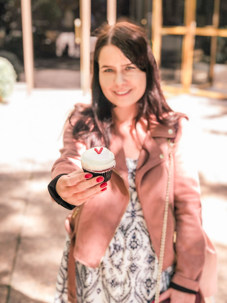 A girl holding a red velvet cupcake from Sprinkles towards the camera