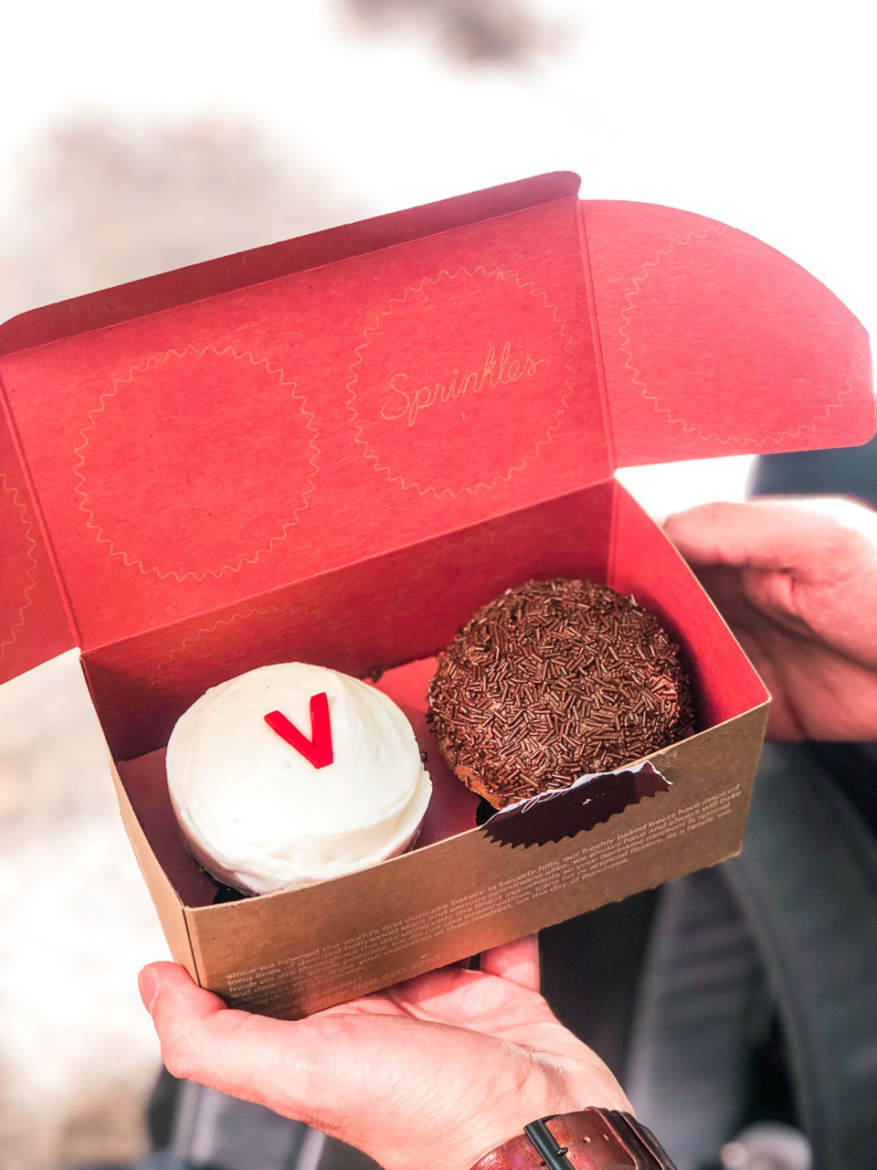 A man holding an open box of Sprinkles cupcakes