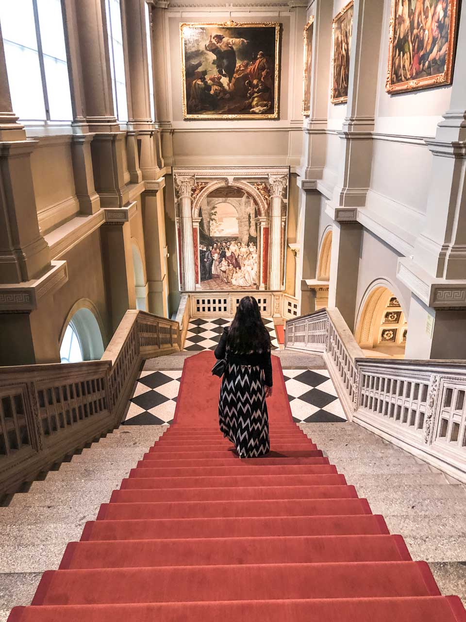 A girl in a maxi dress walking down the stairs inside the Old Masters Picture Gallery in Dresden