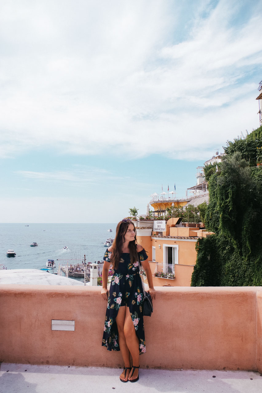 Girl in a floral dress standing in Positano with the Covo dei Saraceni hotel in the background