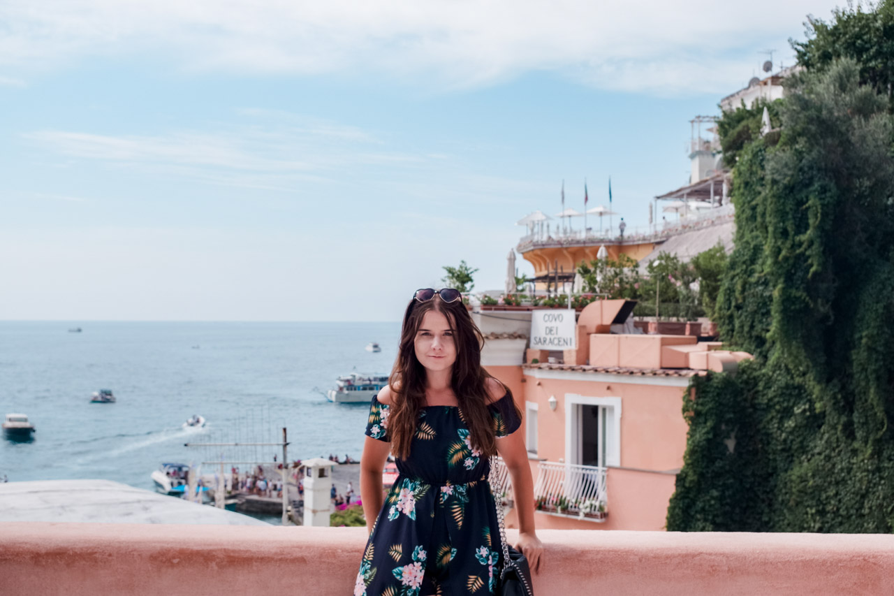 A girl in a floral dress standing in Positano, Italy with the Covo dei Saraceni hotel in the background