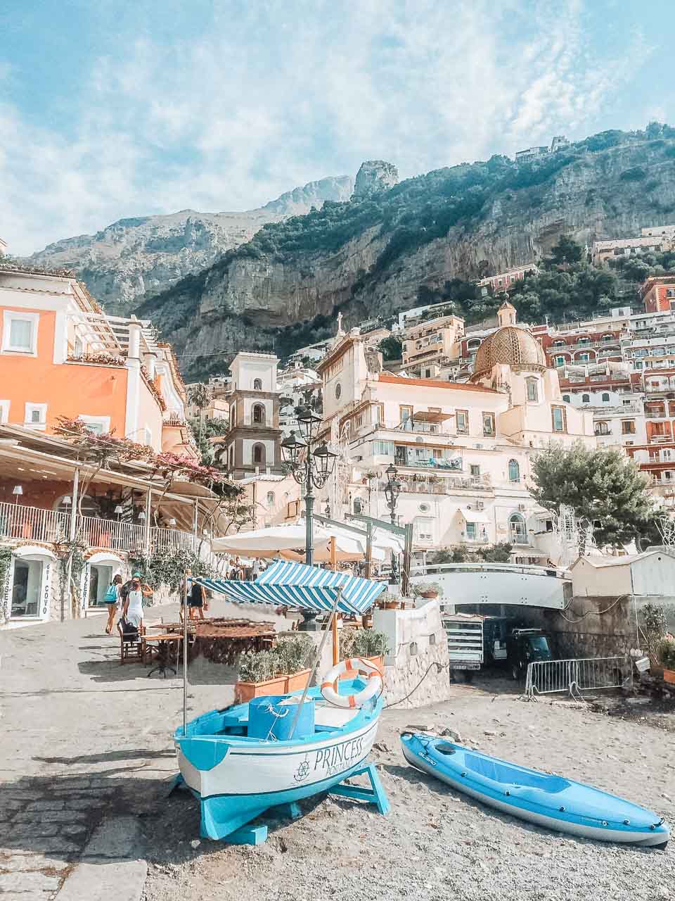 A boat docked on the beach in Positano with hillside houses and mountains in the background