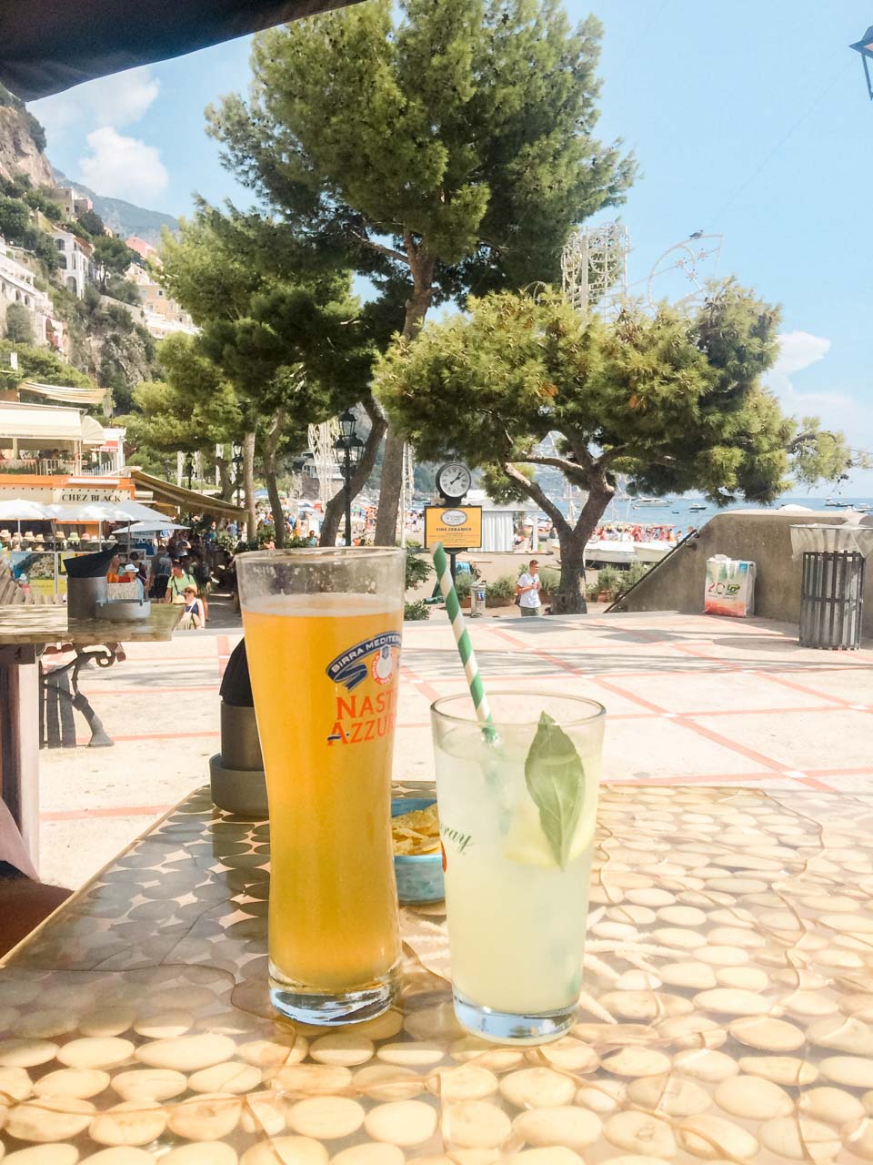 A beer and a cocktail on a table in Positano with Spiaggia Grande in the background