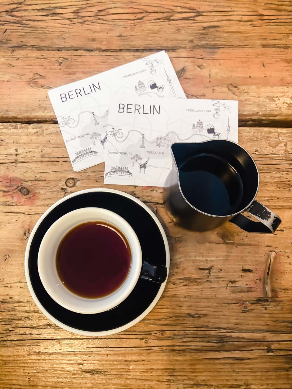 Cup of coffee and a pitcher on a table next to two Berlin postcards inside The Barn Coffee Roasters