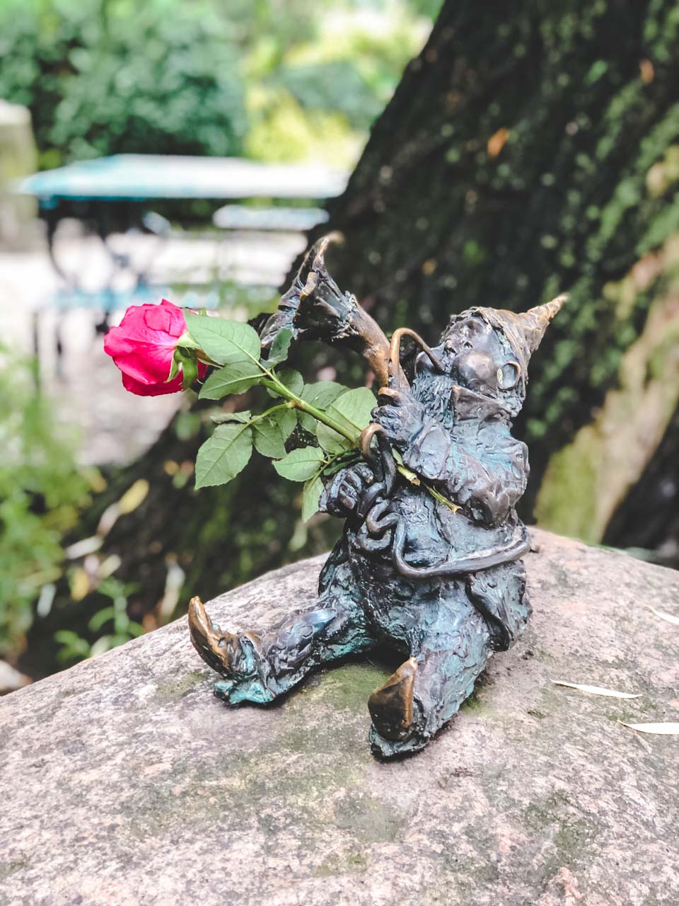 A figurine of a dwarf playing the trumpet with a red rose tucked under his arm