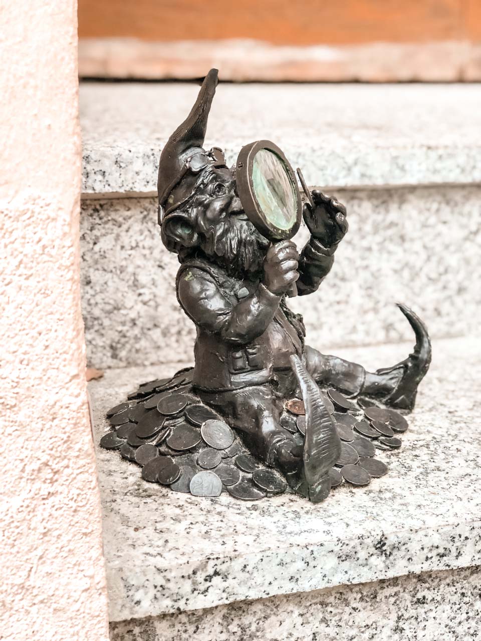 A figurine of a dwarf inspecting coins under a magnifying glass