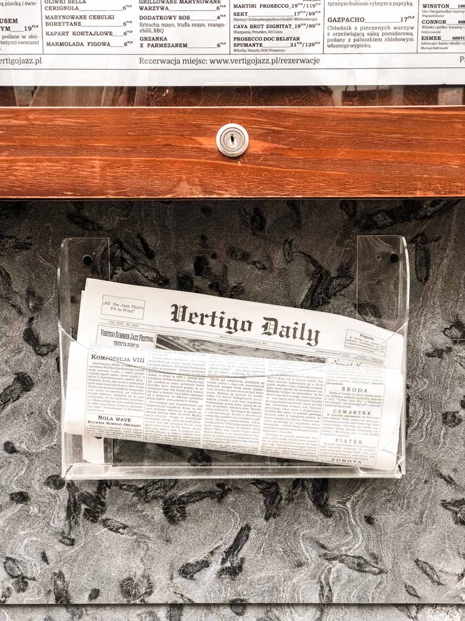 A Vertigo Daily newspaper in a wall-mounted transparent newspaper rack