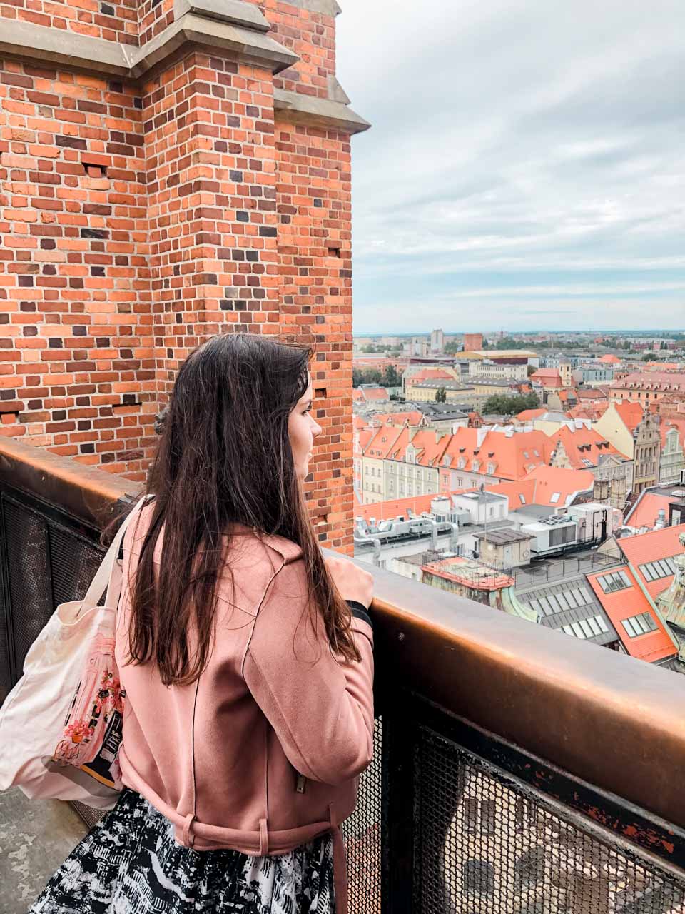 A woman in a pink suede jacket standing on the Penitent Bridge in Wrocław and admiring the views
