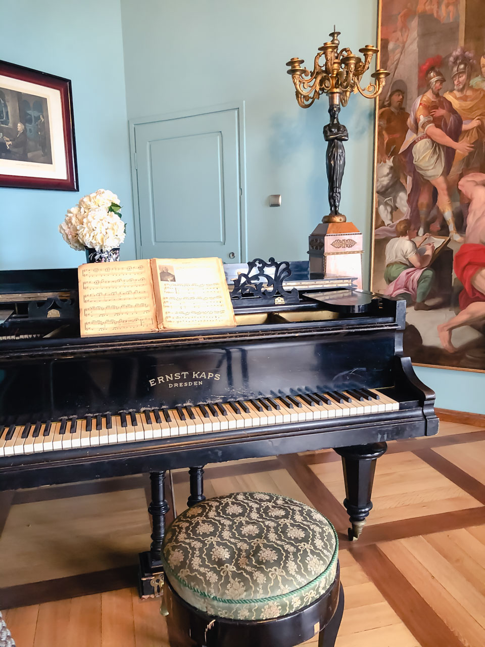 An Ernst Kaps piano with a small round pouf and a piano book inside a blue room at Książ Castle