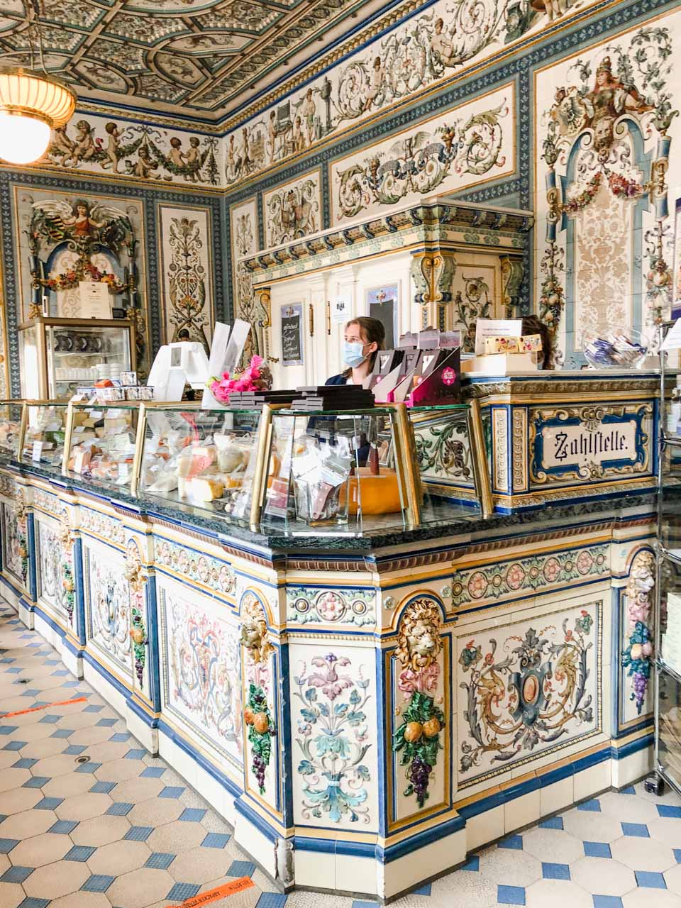 Woman behind a counter decorated with hand-painted tiles inside Pfunds Molkerei in Dresden, Germany