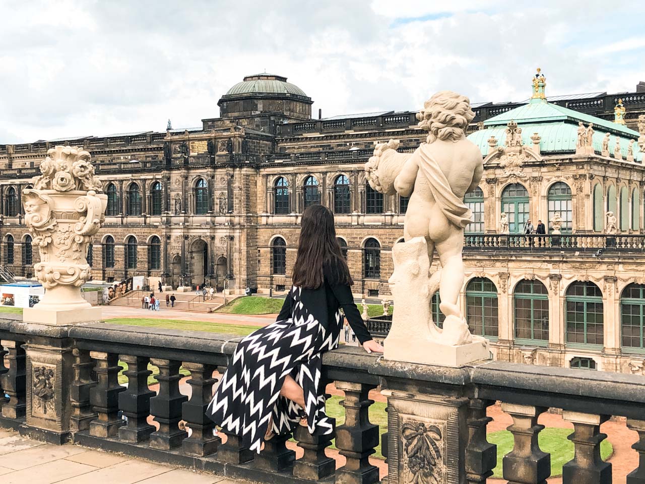 A woman in a black and white maxi dress sitting on a balustrade on the Zwinger terrace in Dresden