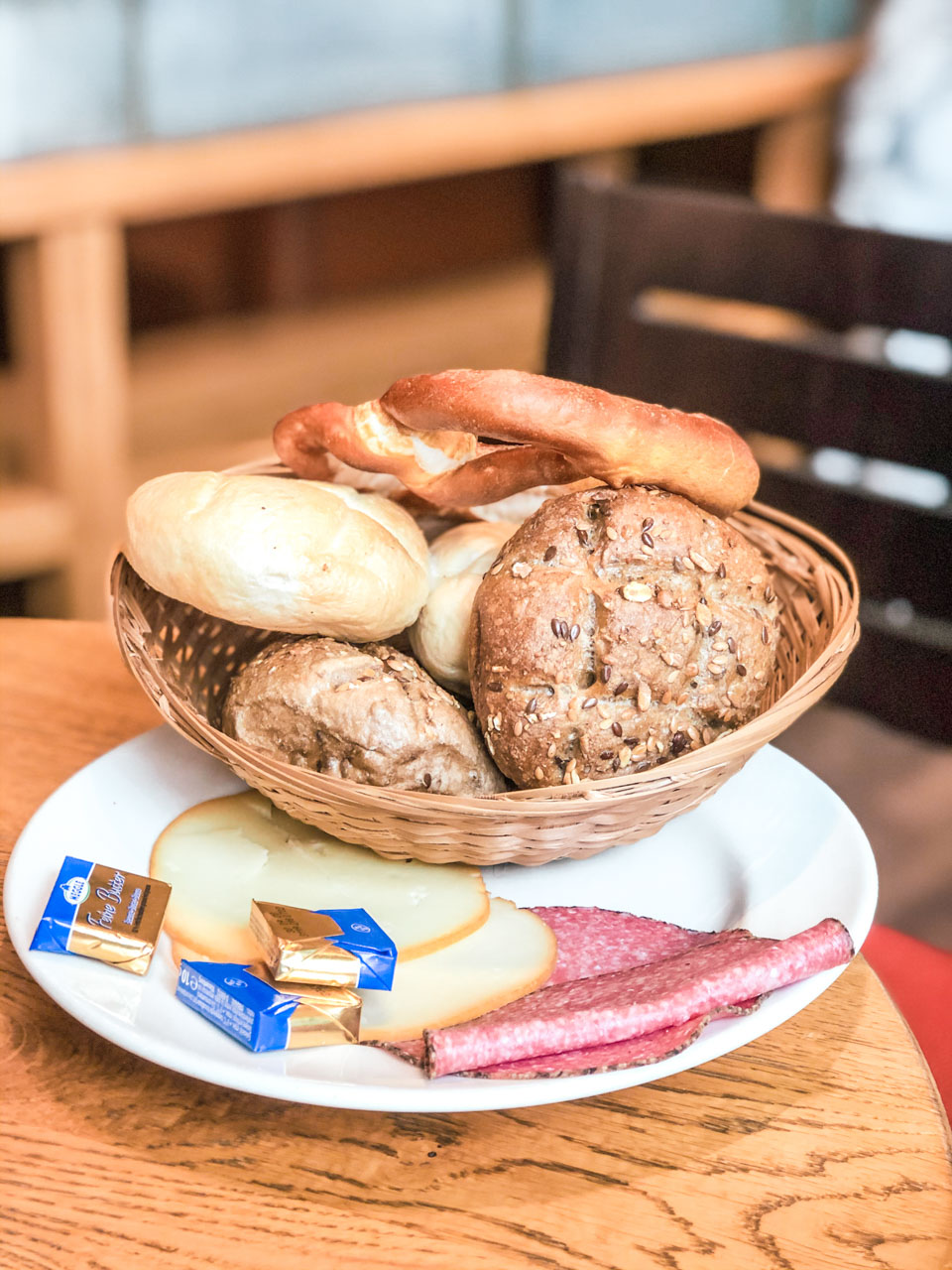 A basket filled with fresh rolls next to mini butter portions and a few slices of cheese and salami