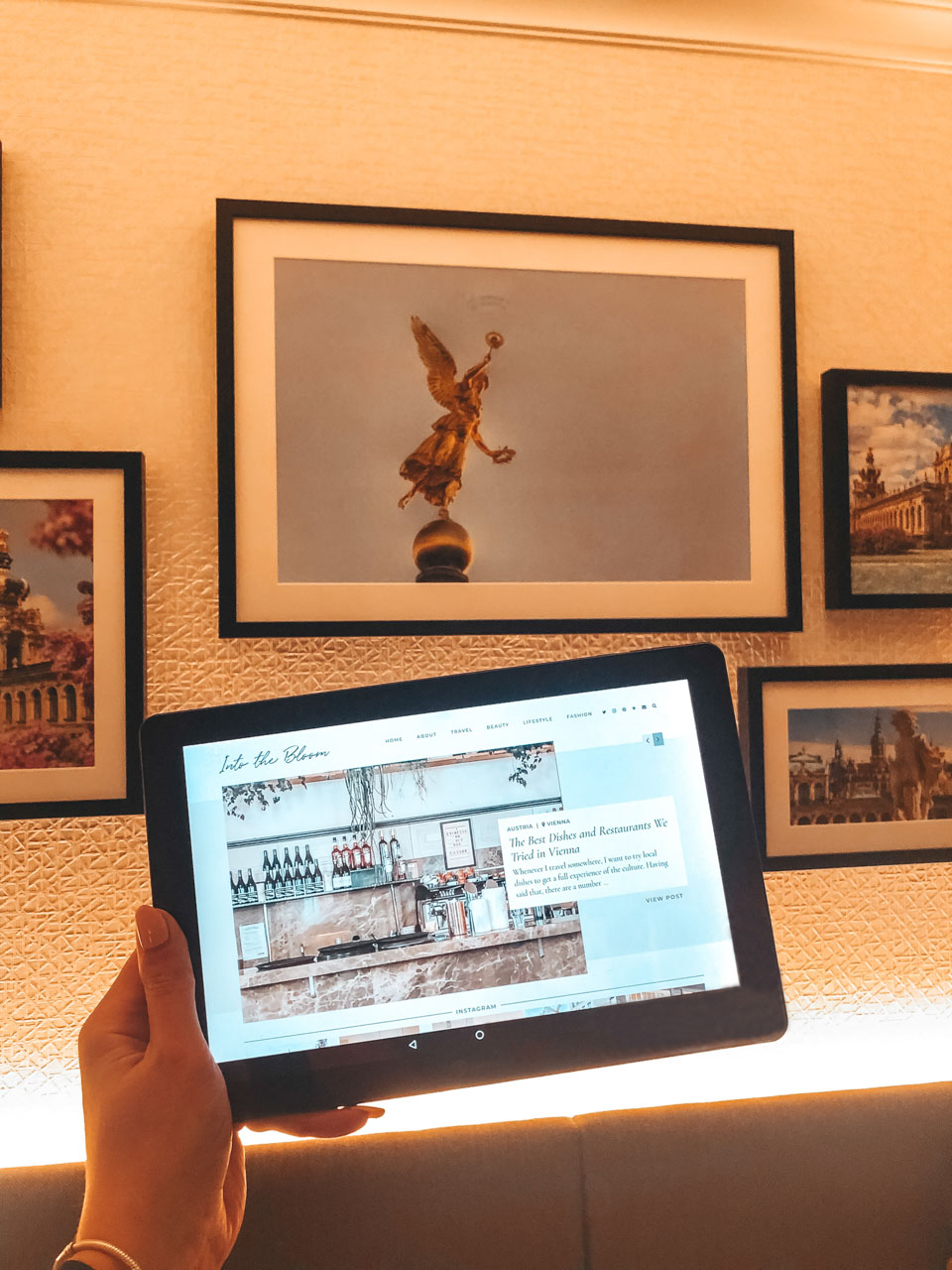 A woman holding up a tablet with a blog open on it with various photos of Dresden in the background