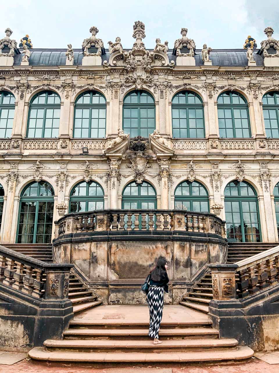 A woman in a black and white maxi dress walking up the stairs outside Zwinger Palace in Dresden