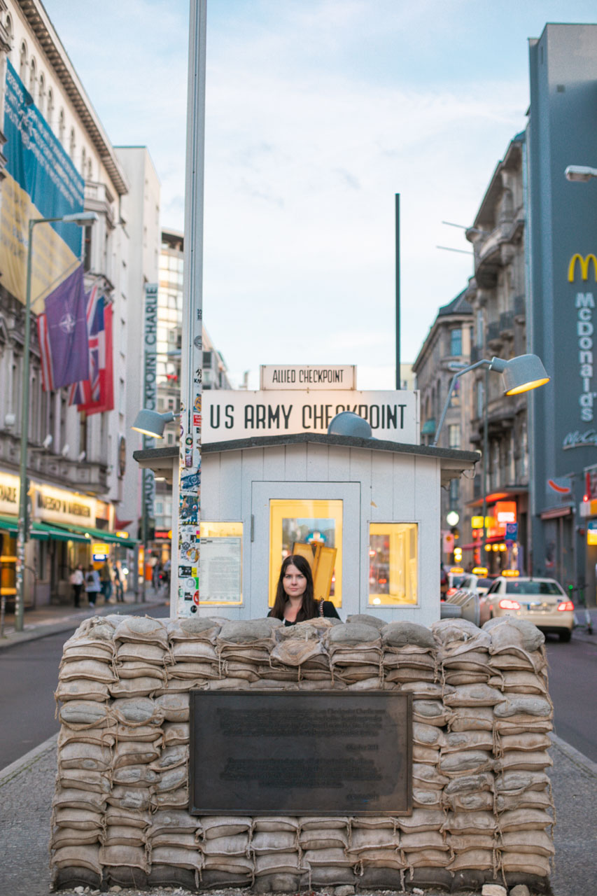 A dark-haired woman standing behind the sandbags at Checkpoint Charlie in Berlin, Germany