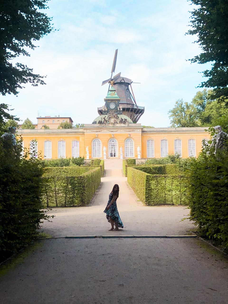 A woman in a maxi dress standing in front of the New Chambers and the Historic Mill of Sanssouci