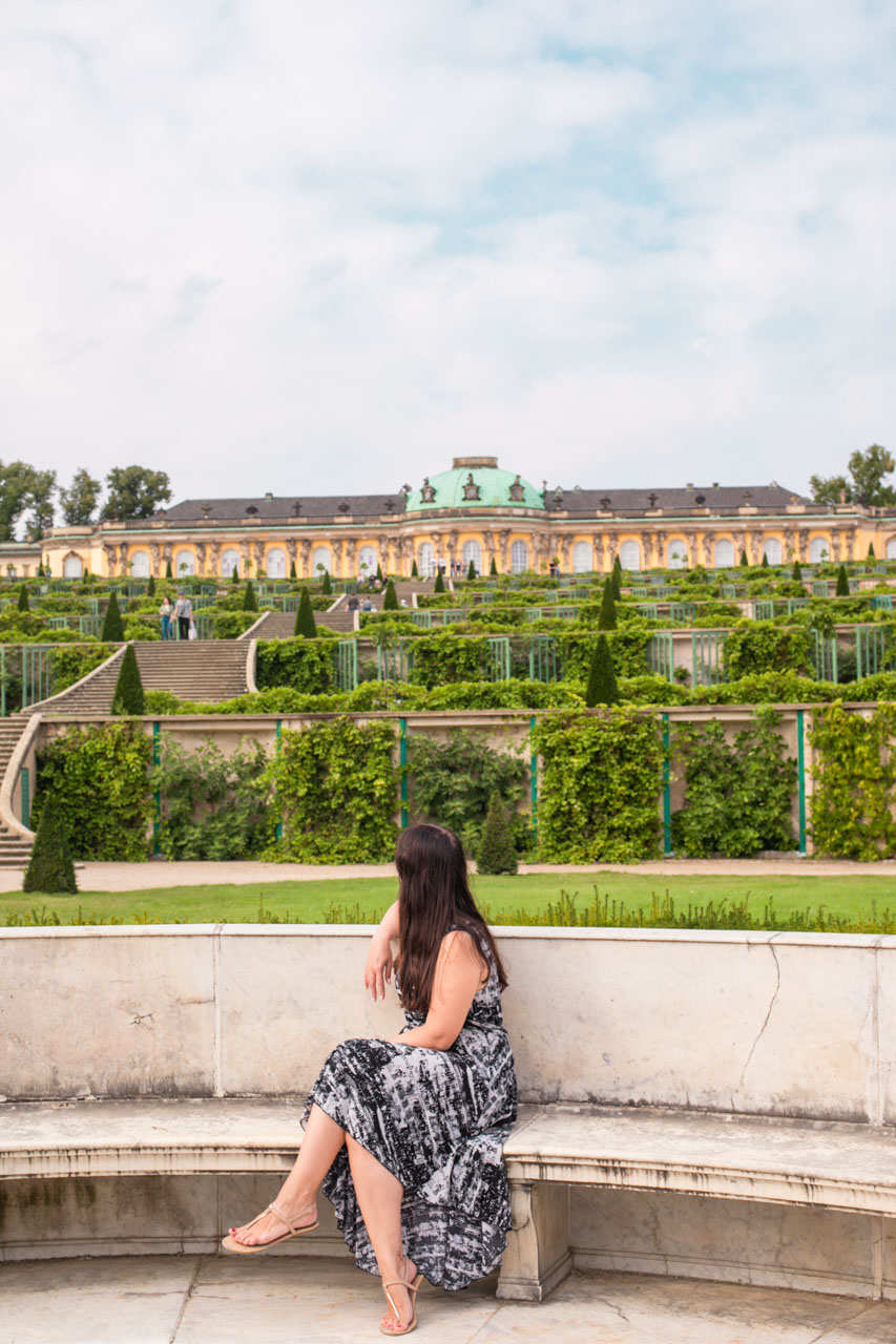 A woman in a black and white maxi dress sitting on the bench looking at Sanssouci Palace