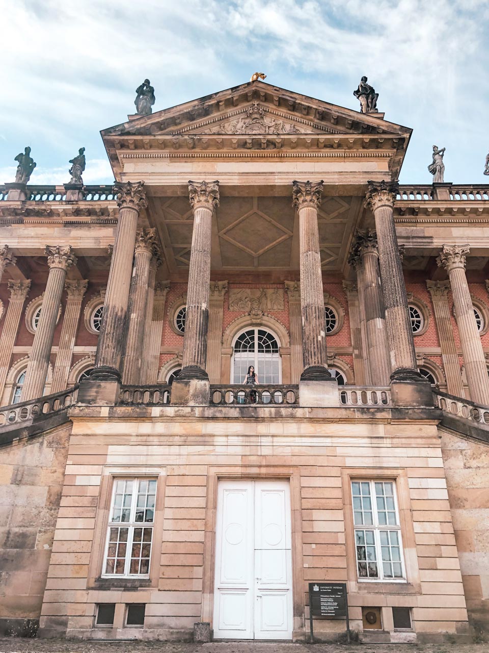 A woman leaning against a balustrade outside the University of Potsdam building at Sanssouci Park