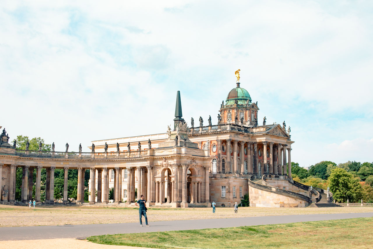 A man standing at Sanssouci Park with the Faculty of Arts of the University of Potsdam behind him