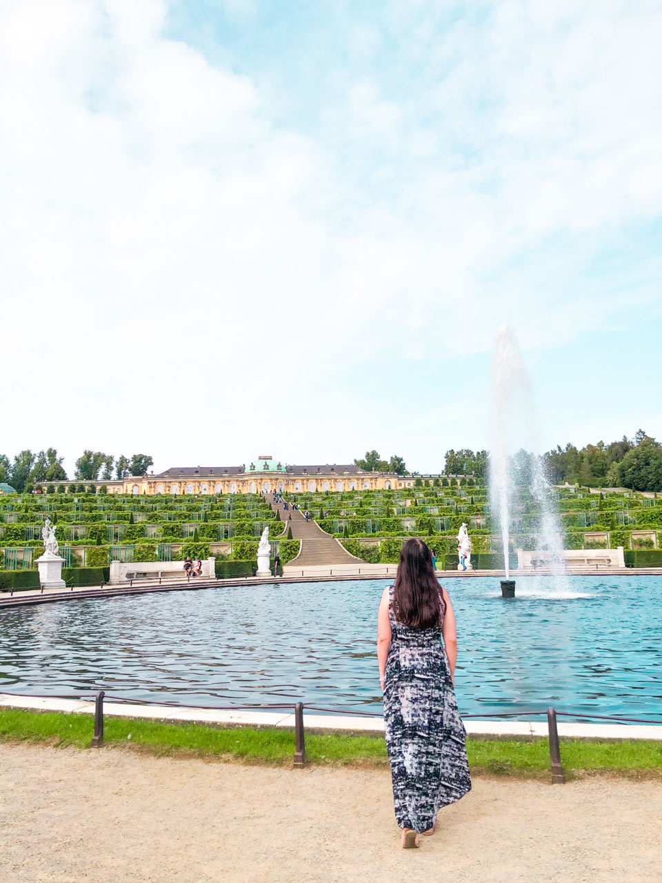 A woman in a black and white maxi dress looking at the fountain in front of Sanssouci Palace