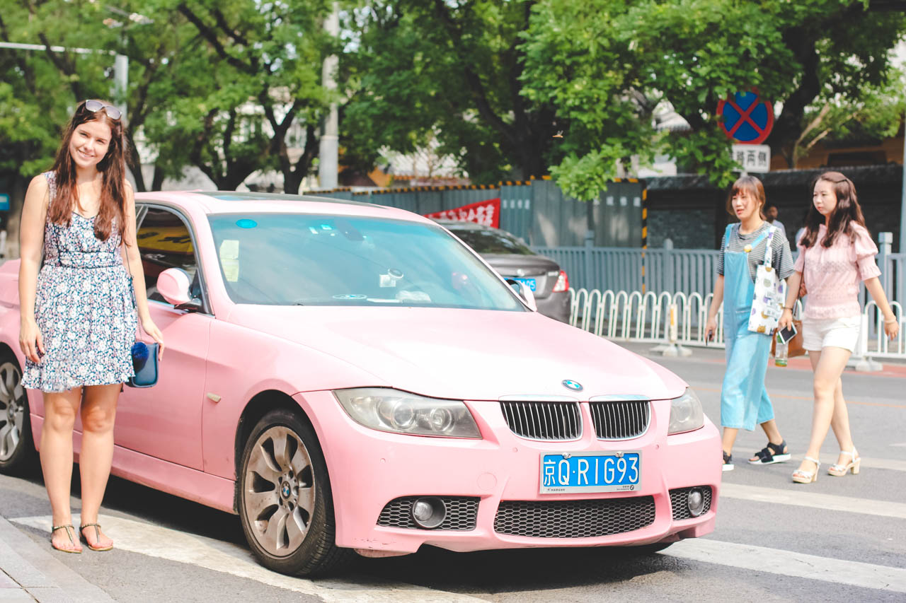 Smiling girl in a floral dress standing next to a pink car in a street in Beijing, China