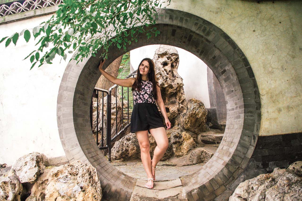 Smiling woman in a playsuit standing at a moon gate at Beihai Park in Beijing, China
