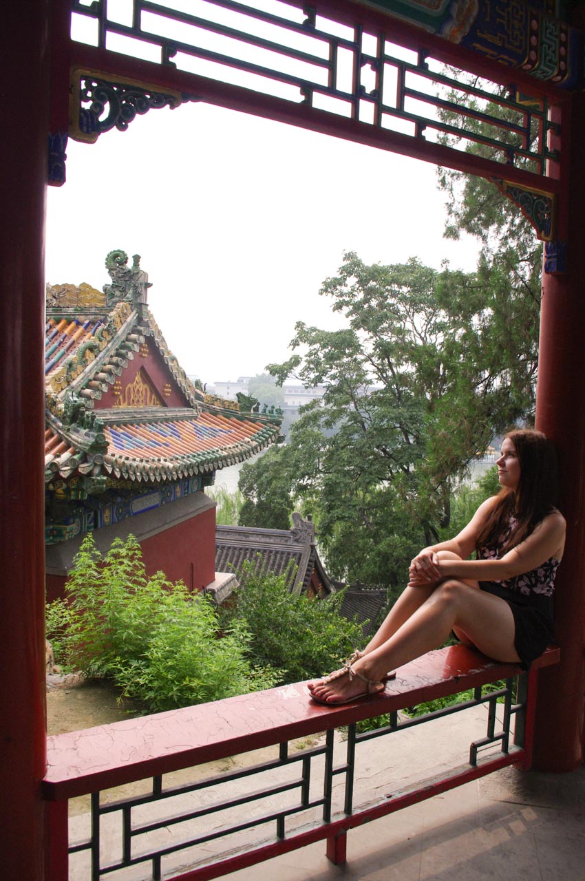 Woman in a playsuit looking upwards as she is sitting on the ledge of a traditional Chinese pavilion