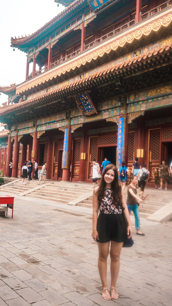 Smiling woman in a playsuit standing in front of a prayer hall at the Yonghegong Lama Temple