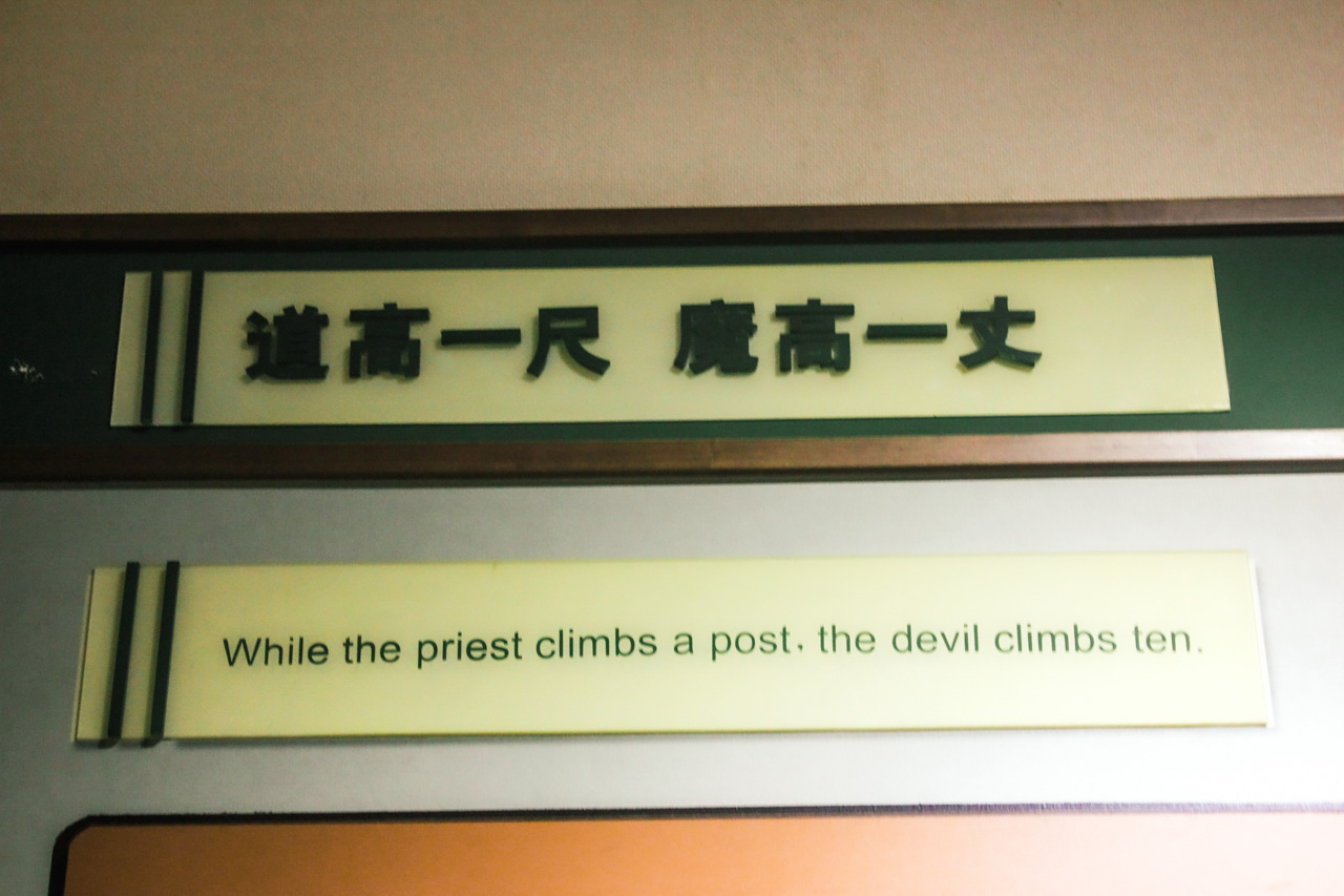 Museum label saying "While the priest climbs a post, the devil climbs then" with Chinese translation