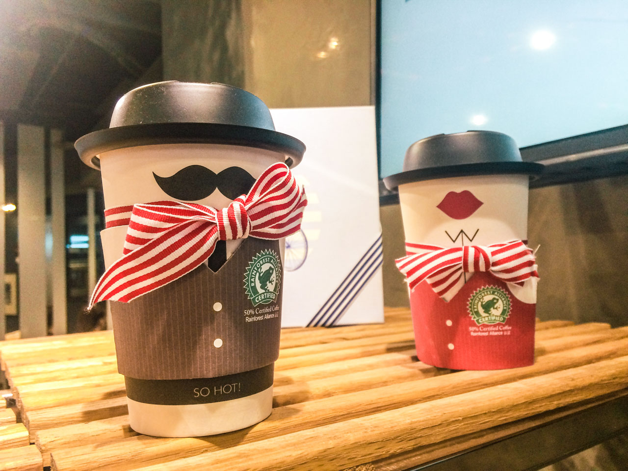 Two paper coffee cups with red lips and a moustache drawn on them to look like a man and a woman