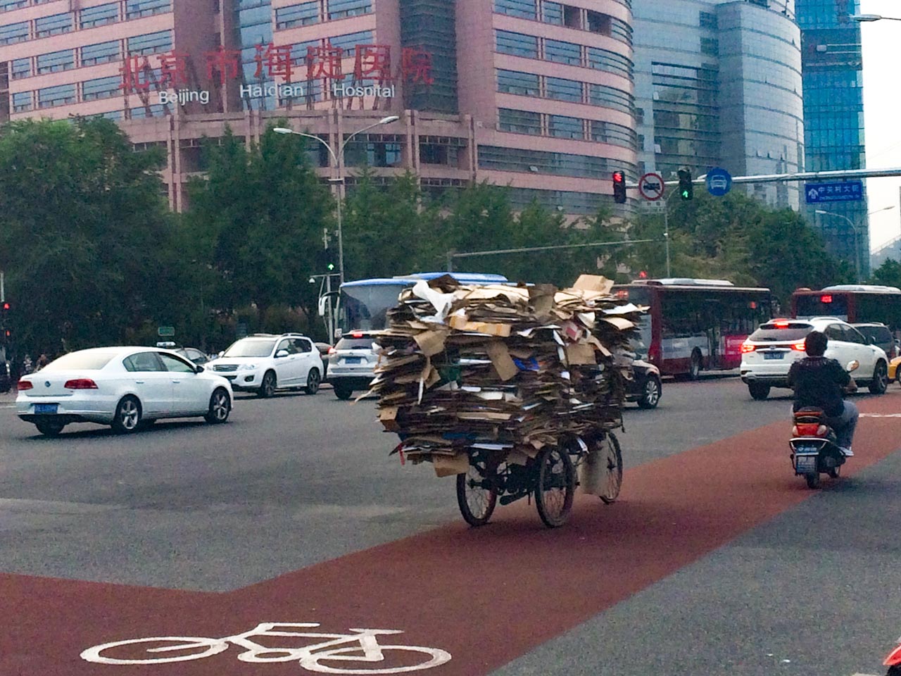 A Chinese man on a tricycle carrying high piles of cardboard waste