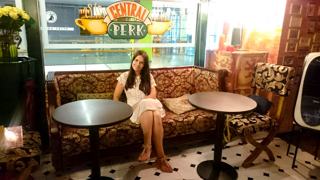 Smiling girl in a white lace dress sitting on a sofa inside the Friends Café in Beijing