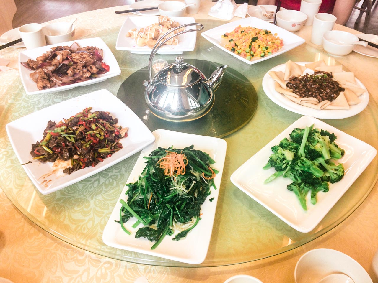 Different Chinese dishes on a Lazy Susan rotating table with a metal teapot in the middle